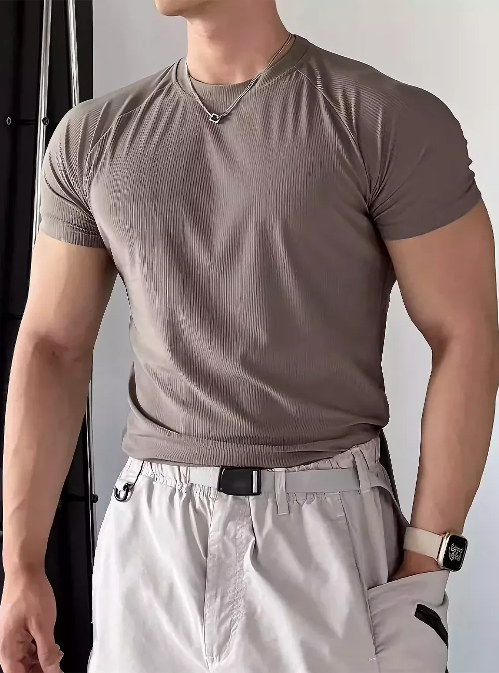 棕色涼感羅紋男短T側面,搭配白褲,淺色牆背景