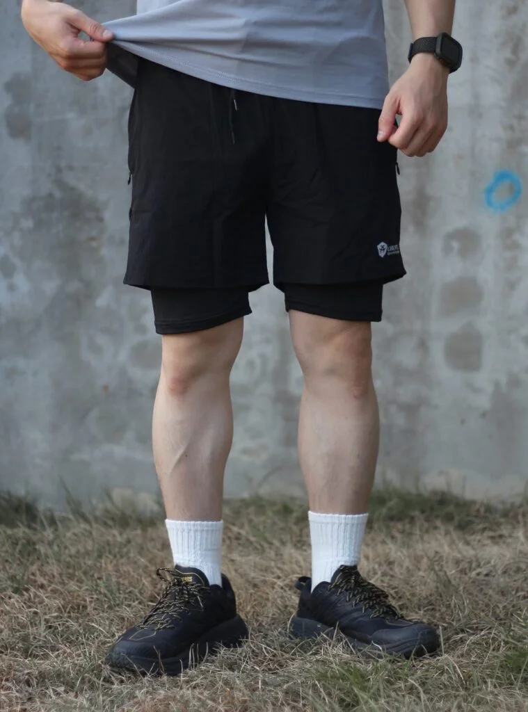 戰術彈力健身短褲黑色 自家實拍 水泥牆前撩起上衣展示腰頭與雙層設計